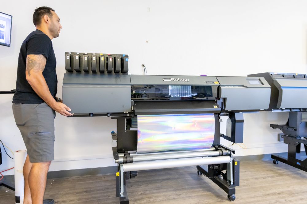 Man standing next to a large inkjet printer in an indoor setting